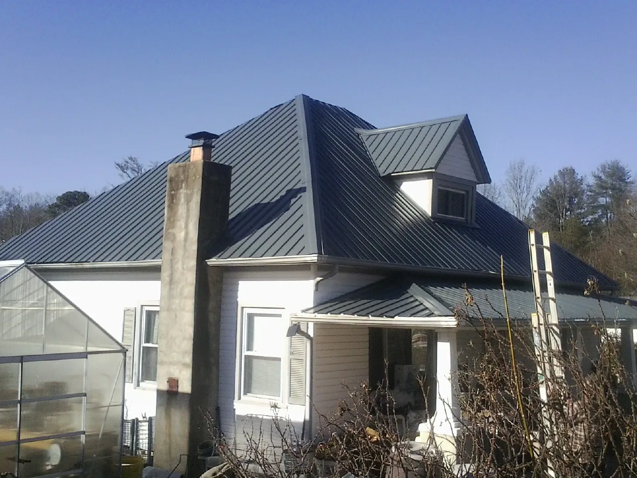 Dark blue standing seam metal roof on a white farmhouse with dormer — Slate & Tile Roof Repair by Roofing Brothers in Winsted