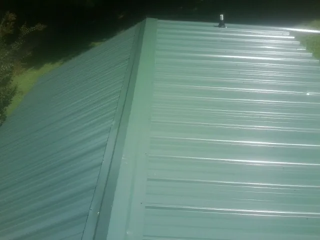 New green metal panels meeting at the ridge of a roof — Flat Roof Repair work by our crew in Winsted