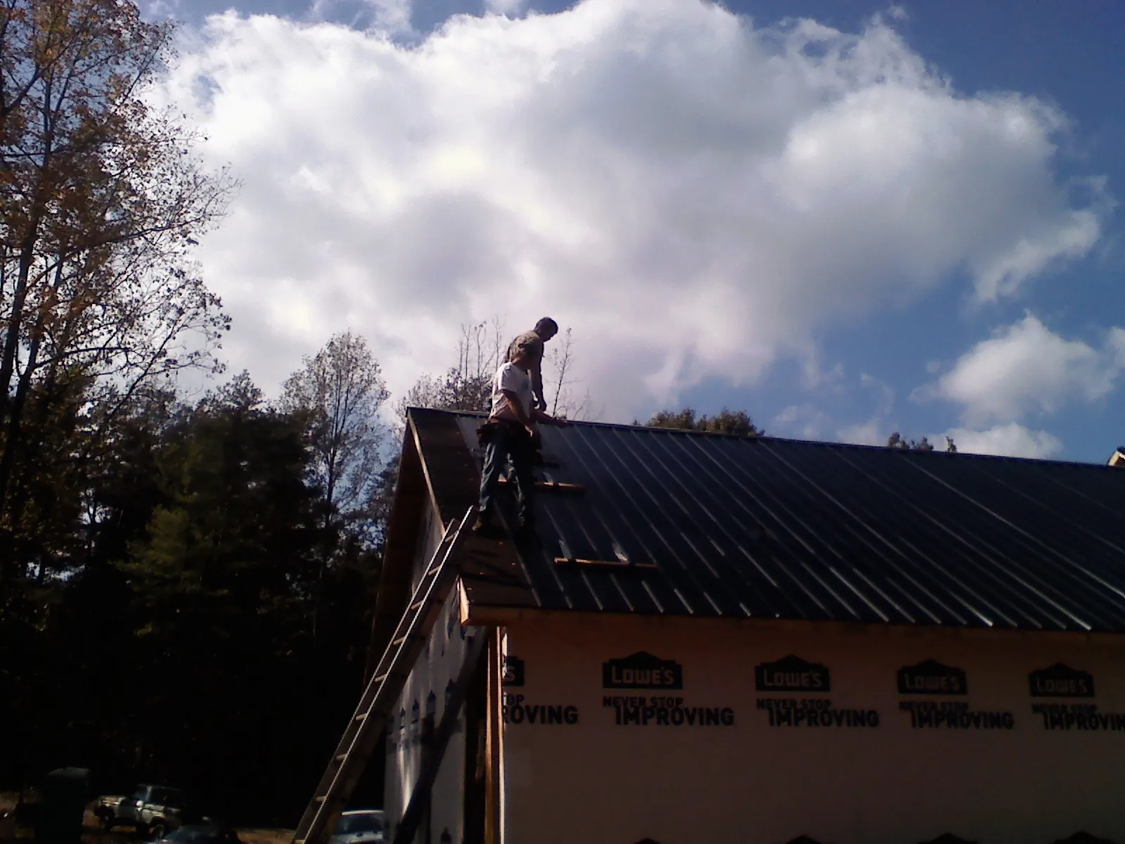 Roofer fastening dark metal panels high against a cloudy sky, from a Roof Inspection job in Winsted