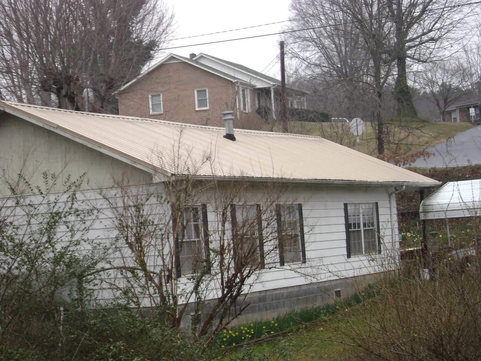 Tan metal roof on a white sided house set into a hillside — Commercial Roofing by Roofing Brothers in Winsted